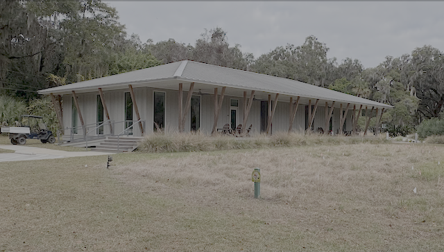 A one-story building with a grassy field in front and a golf cart to the left
