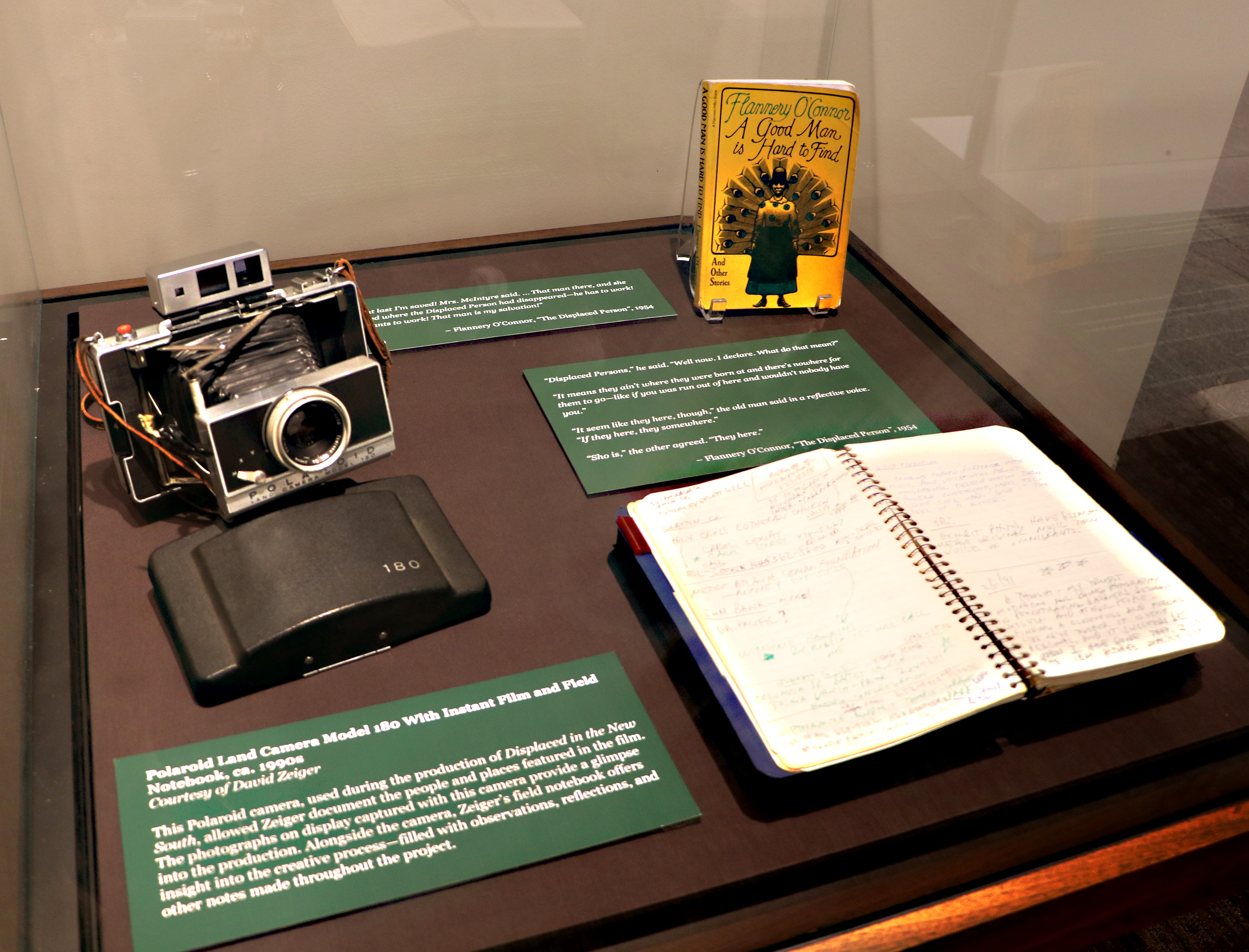 Exhibit case with old Polaroid camera and open notebook