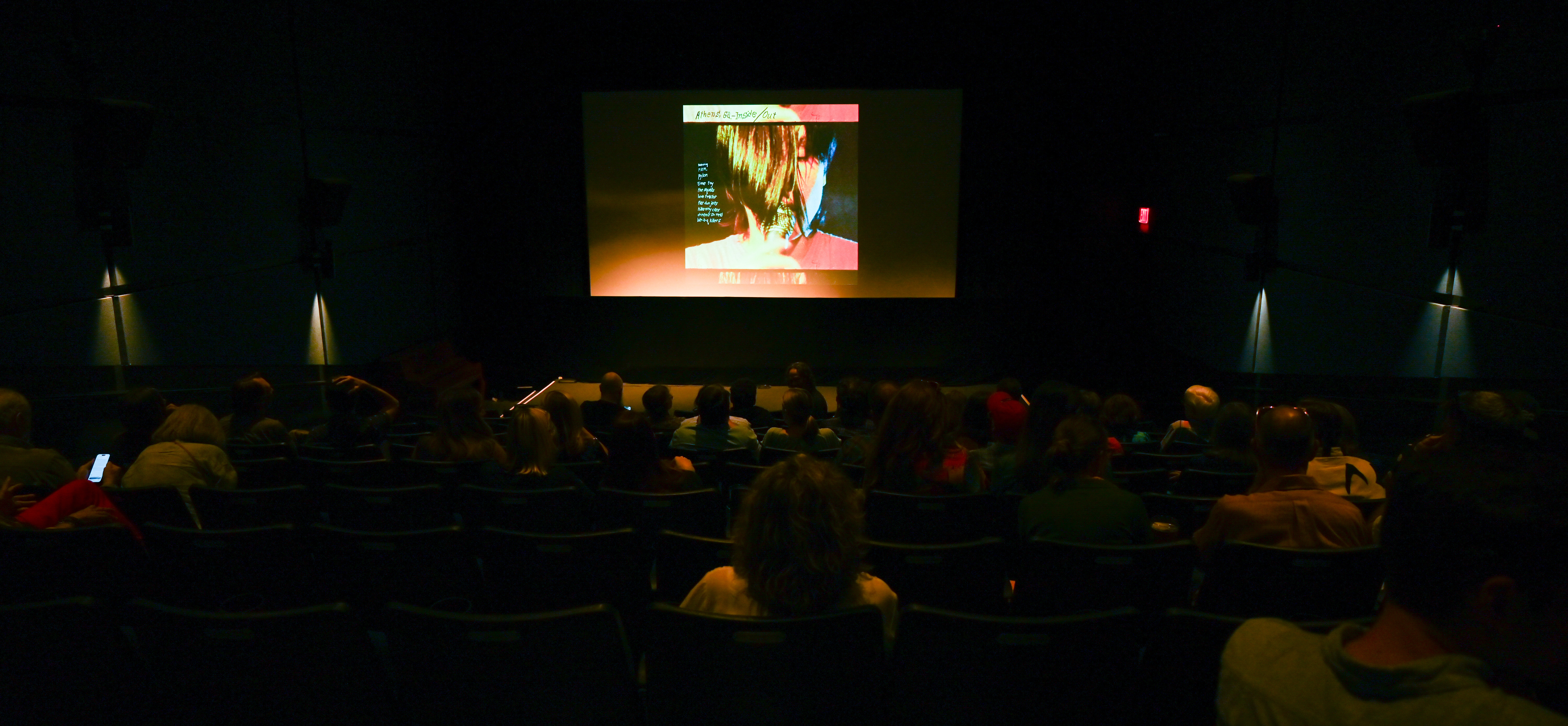 A dark theater with an audience viewing the opening of Athens GA: Inside/Out