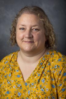 Curly haired blonde woman wearing a yellow floral patterned shirt