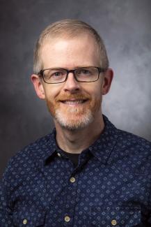 Man with pale red hair wearing glasses and a dark blue shirt.