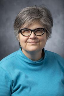 Woman with short hair wearing glasses and an aqua turtleneck.