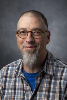 Man with long goatee, who's wearing a plaid shirt and glasses