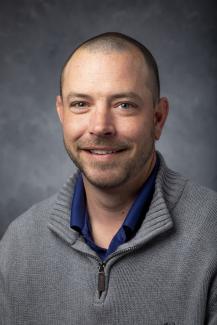 Man wearing a grey sweater over a blue shirt.