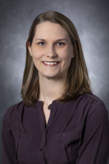 Woman with shoulder length dark blonde hair wearing a dark purple button-up shirt.