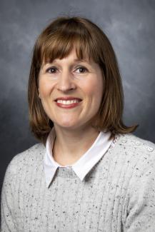 Woman with shoulder length brown hair wearing a white shirt under a light grey sweater