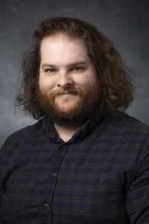 Man in plaid shirt with beard and shoulder length curly brown hair