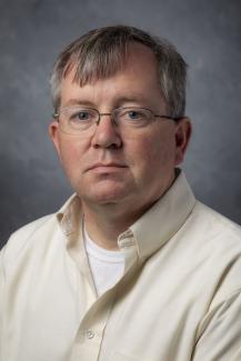 Short haired man wearing glasses and a cream colored shirt.
