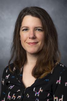 Woman with brown hair just past her shoulders. She's wearing a black shirt with multicolored llamas printed on it.