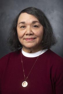 Woman with chin length dark hair. She's wearing a white shirt under a dark red sweater. 