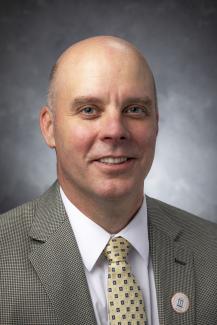 Man with blue eyes wearing a yellow spotted tie and light jacket.