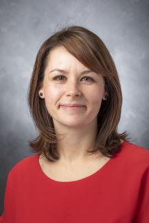 Woman with brown hair and red shirt with sideswept bangs.