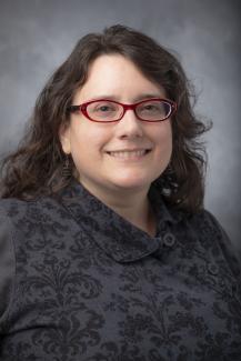 Woman with glasses and long brown hair wearing a charcoal turtleneck sweater.