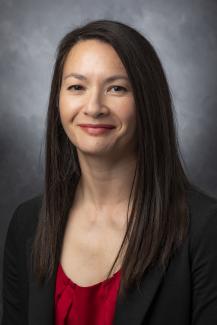 Woman with long dark hair wearing a red shirt and black jacket.