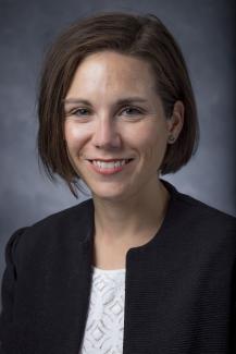 woman with short dark hair wearing a black jacket and white shirt.