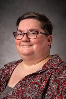 Woman with short dark hair and glasses, smiling and wearing a maroon paisley shirt