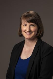 woman with bangs, smiling and wearing a blue shirt and black cardigan