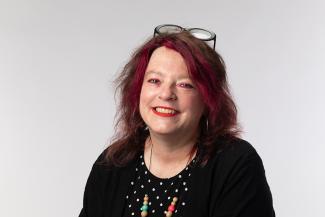 Woman smiling with glasses on her head and a dark shirt and necklace.