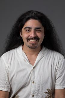 Man with white button up shirt, mustache, and long hair smiling