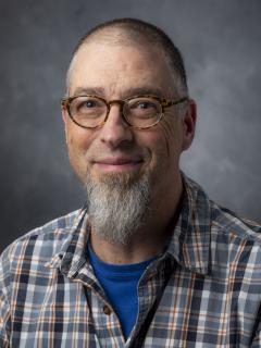 Man with long goatee, who's wearing a plaid shirt and glasses