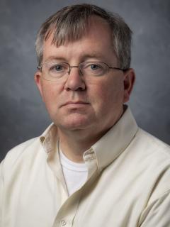 Short haired man wearing glasses and a cream colored shirt.