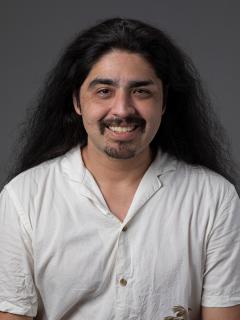 Man with white button up shirt, mustache, and long hair smiling